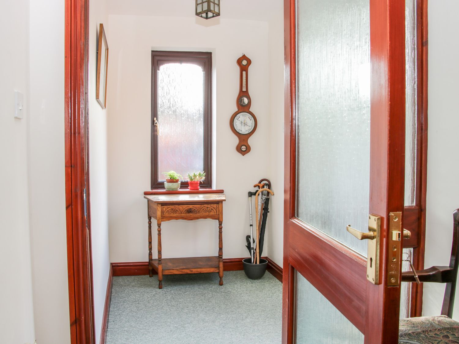 A hallway with a wooden table and two small plants under a textured window at Court Farm in Neen Sollars near Cleobury Mortimer