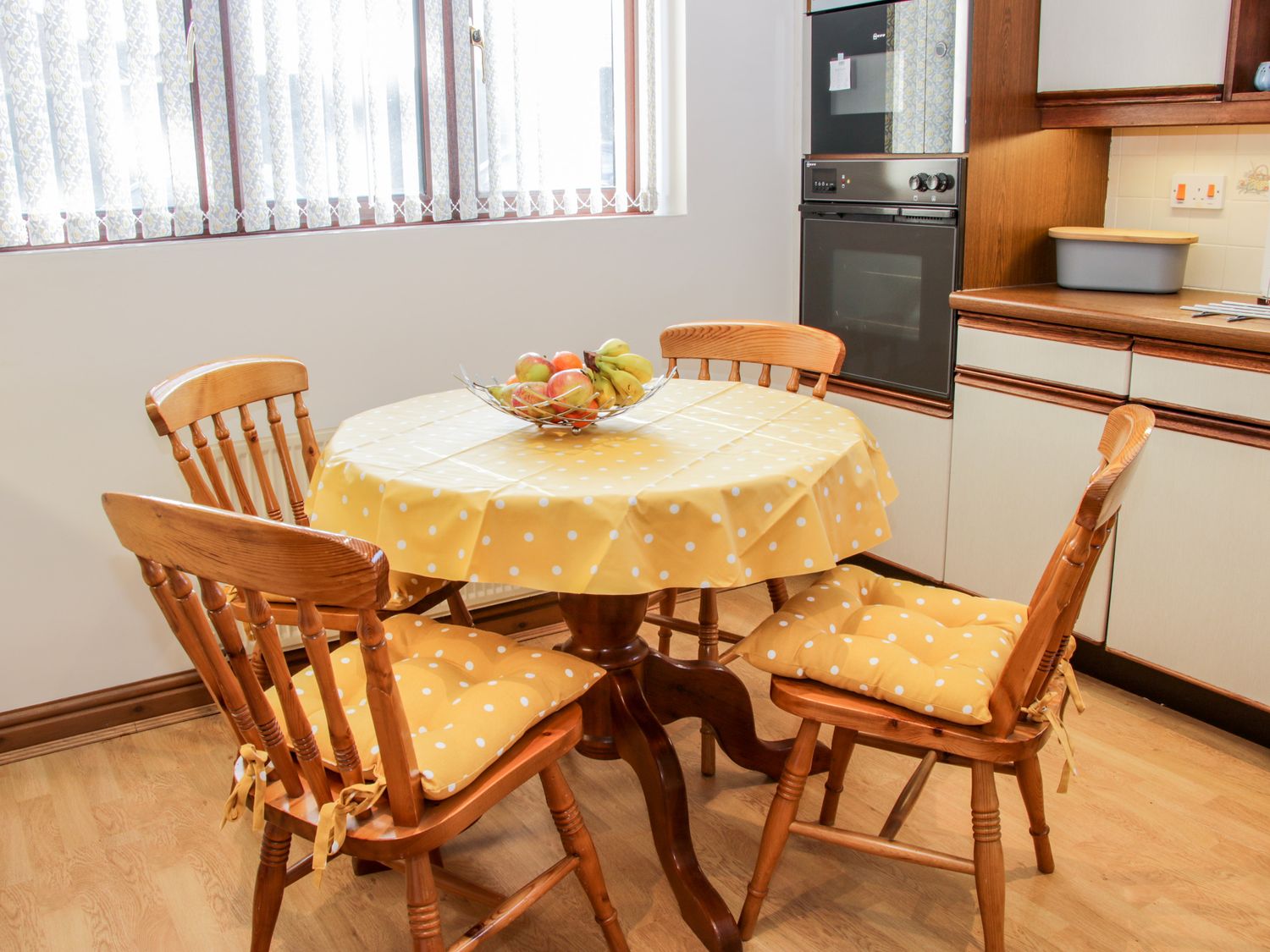 A kitchen with a round table covered with a yellow polka dot tablecloth and four wooden chairs with matching cushions at Court Farm Neen Sollars near Cleobury Mortimer