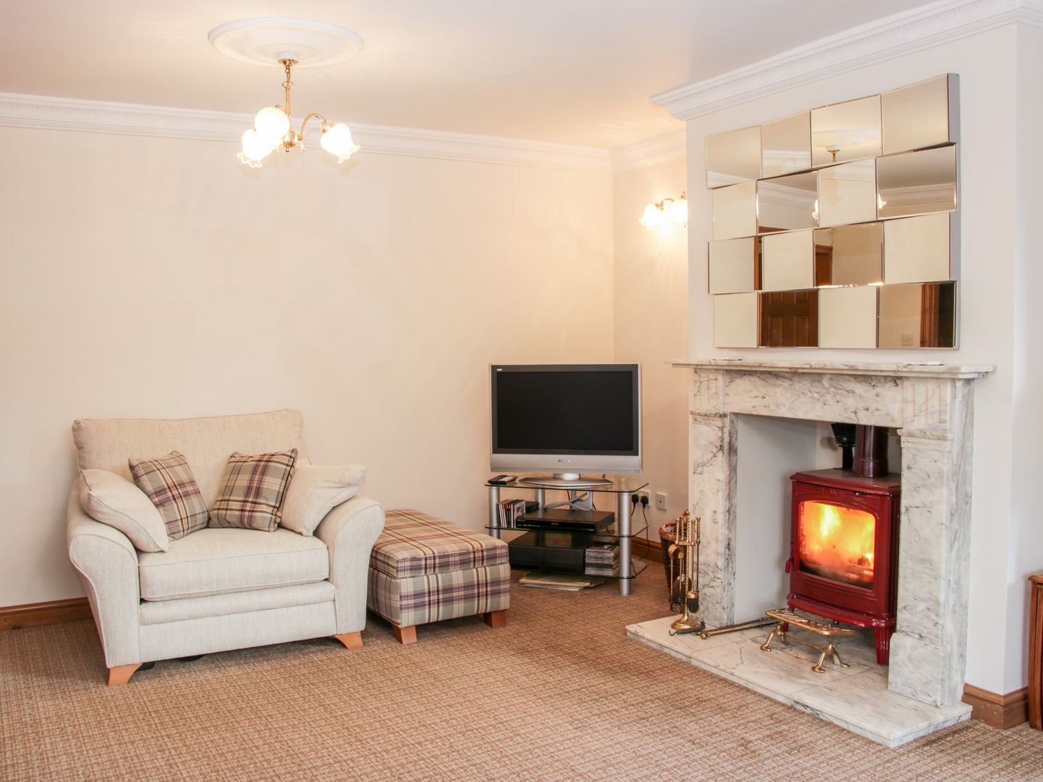 A sitting room with an armchair plaid cushions ottoman a television and a fireplace at Court Farm in Neen Sollars near Cleobury Mortimer