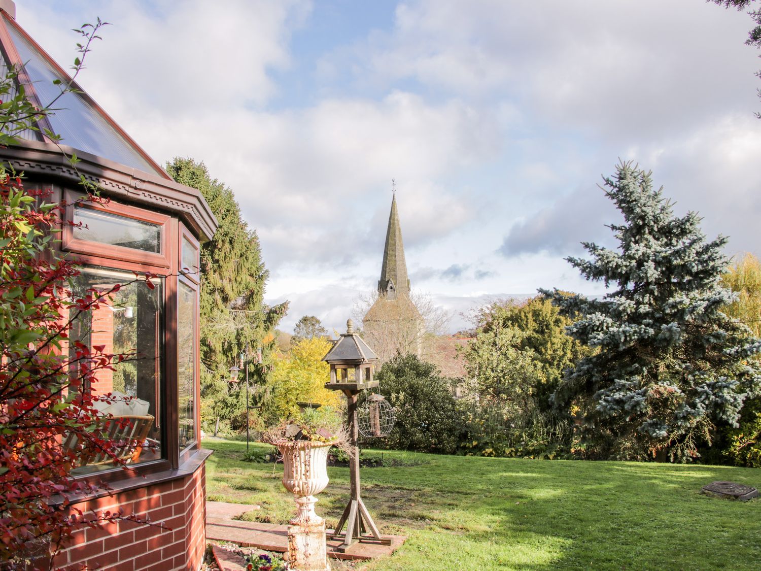 A garden with a bird feeder, trees, and a church steeple in the background at Court Farm in Neen Sollars near Cleobury Mortimer