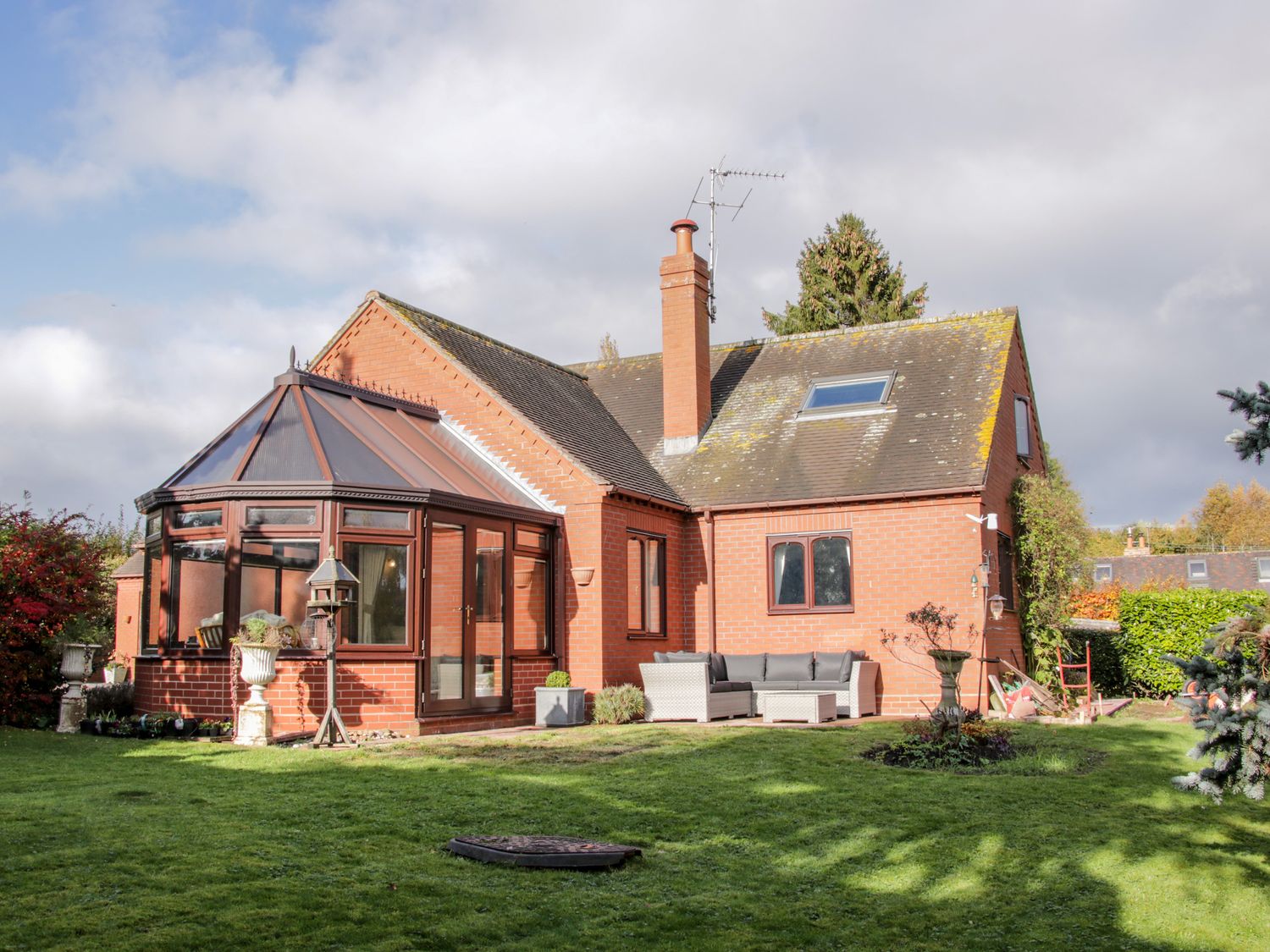 A brick house with a conservatory and outdoor seating on a lawn at Court Farm Neen Sollars near Cleobury Mortimer