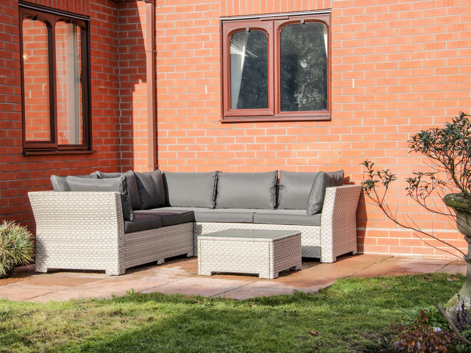 An outdoor patio area with a sectional wicker sofa and a matching coffee table against a brick wall at Court Farm in Neen Sollars near Cleobury Mortimer