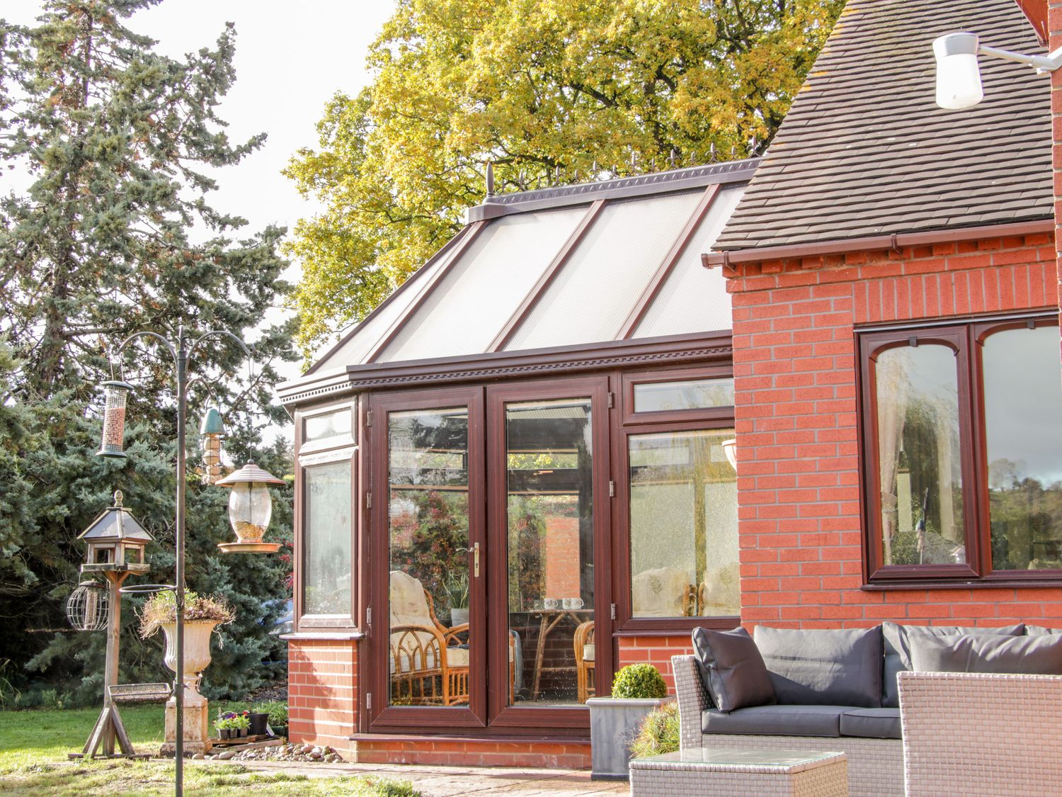 A brick conservatory with glass doors and windows next to an outdoor sofa set and bird feeders at Court Farm in Neen Sollars near Cleobury Mortimer