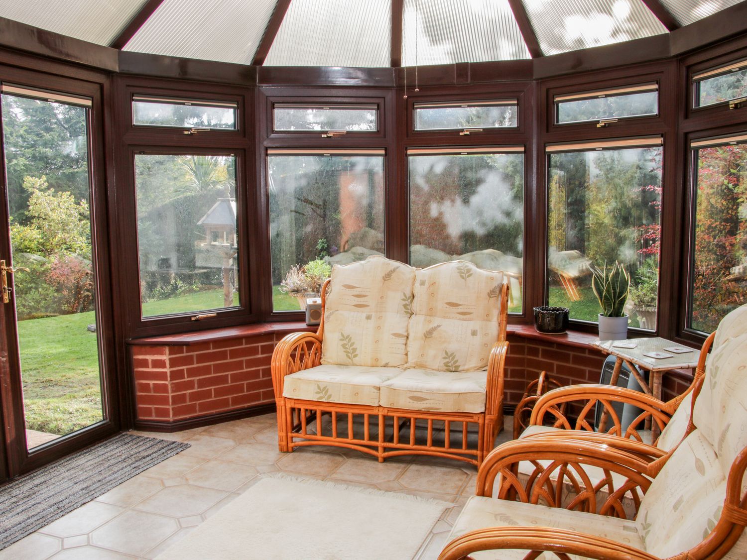 A conservatory with wicker furniture including a sofa and chairs and windows overlooking a garden at Court Farm in Neen Sollars near Cleobury Mortimer