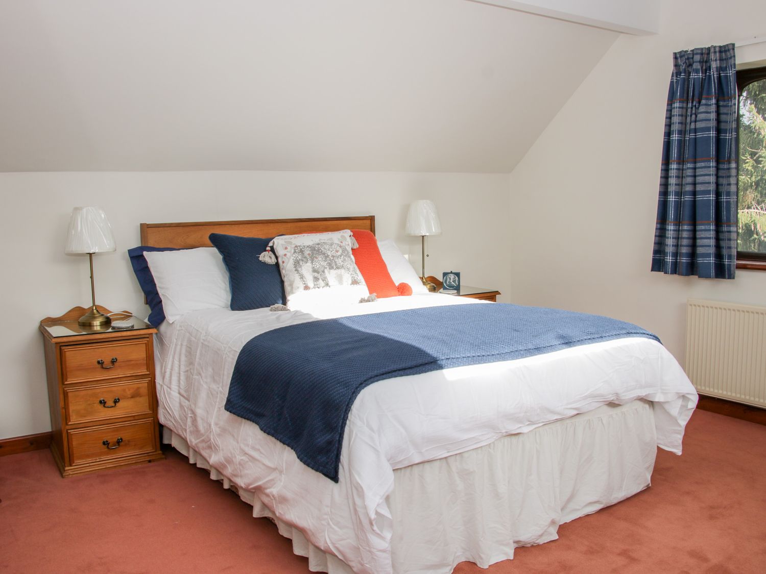 A bedroom with a bed with blue and orange pillows two bedside tables with lamps and a window with blue curtains at Court Farm in Neen Sollars near Cleobury Mortimer