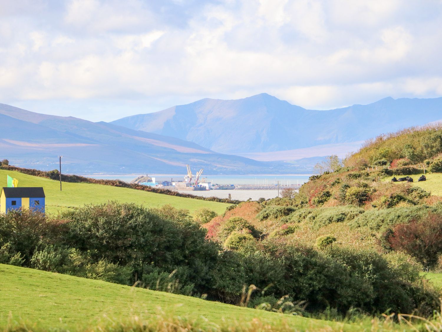A green countryside landscape with a small blue and yellow shed and mountains in the background at The Blue Annex in The Spa near Tralee County Kerry
