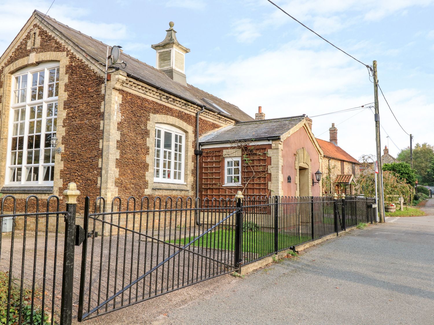 A street view of a stone building with large windows and a black metal fence at The Old School in Downham Market