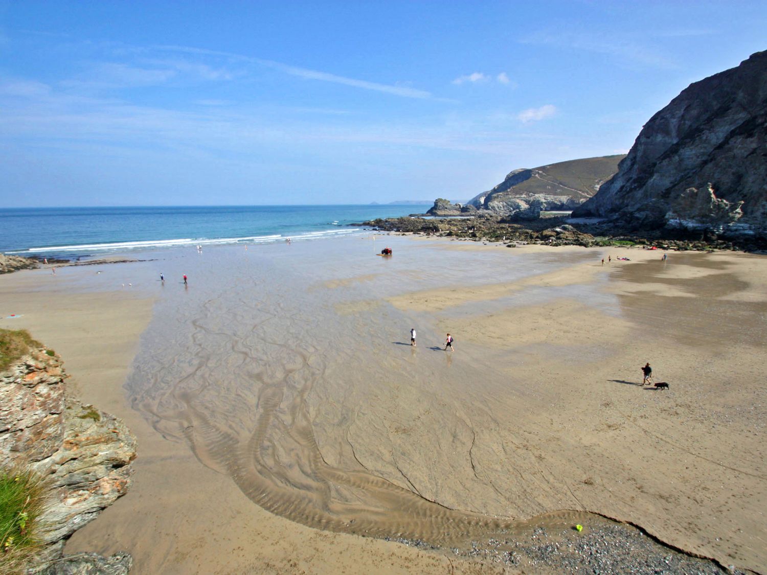 A sandy beach with people walking and rocky cliffs by the sea at Idlewild 2 Wheal Turnavore in St Agnes