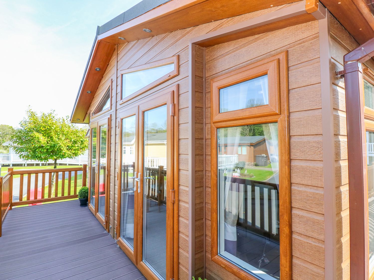 A wooden deck with railing and glass doors attached to a building at Serendipity - Heritage Park Stepaside near Kilgetty