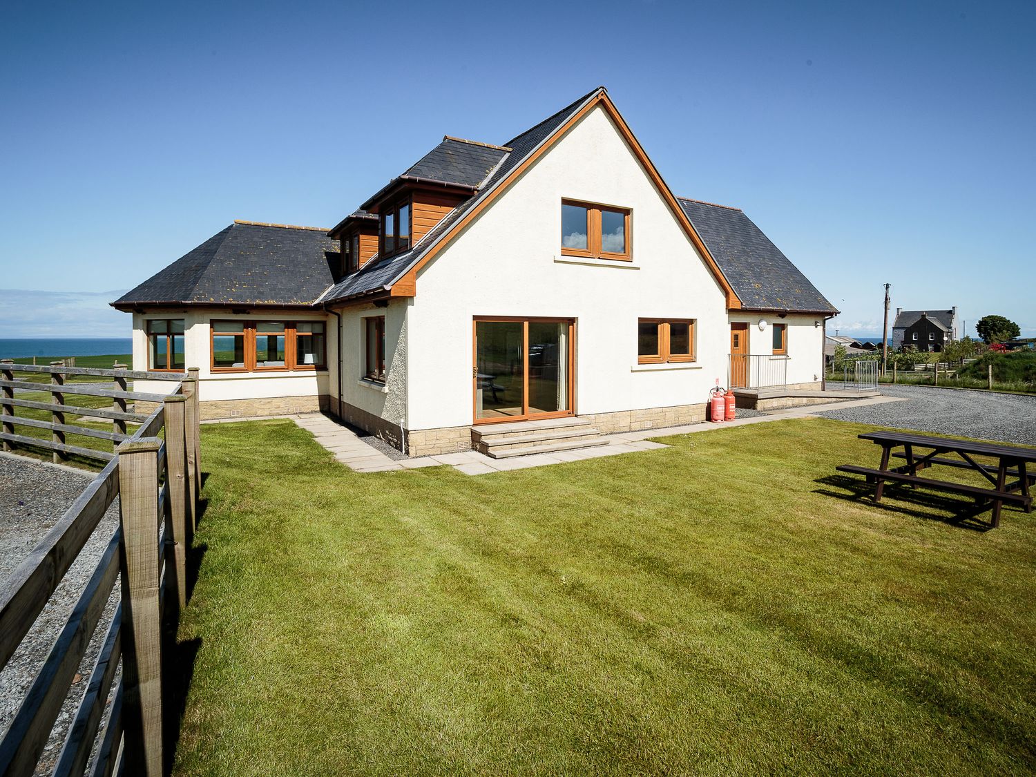 A large house with a grass yard a wooden fence and a picnic table at Corsewall Castle Farm Lodges in Kirkcolm