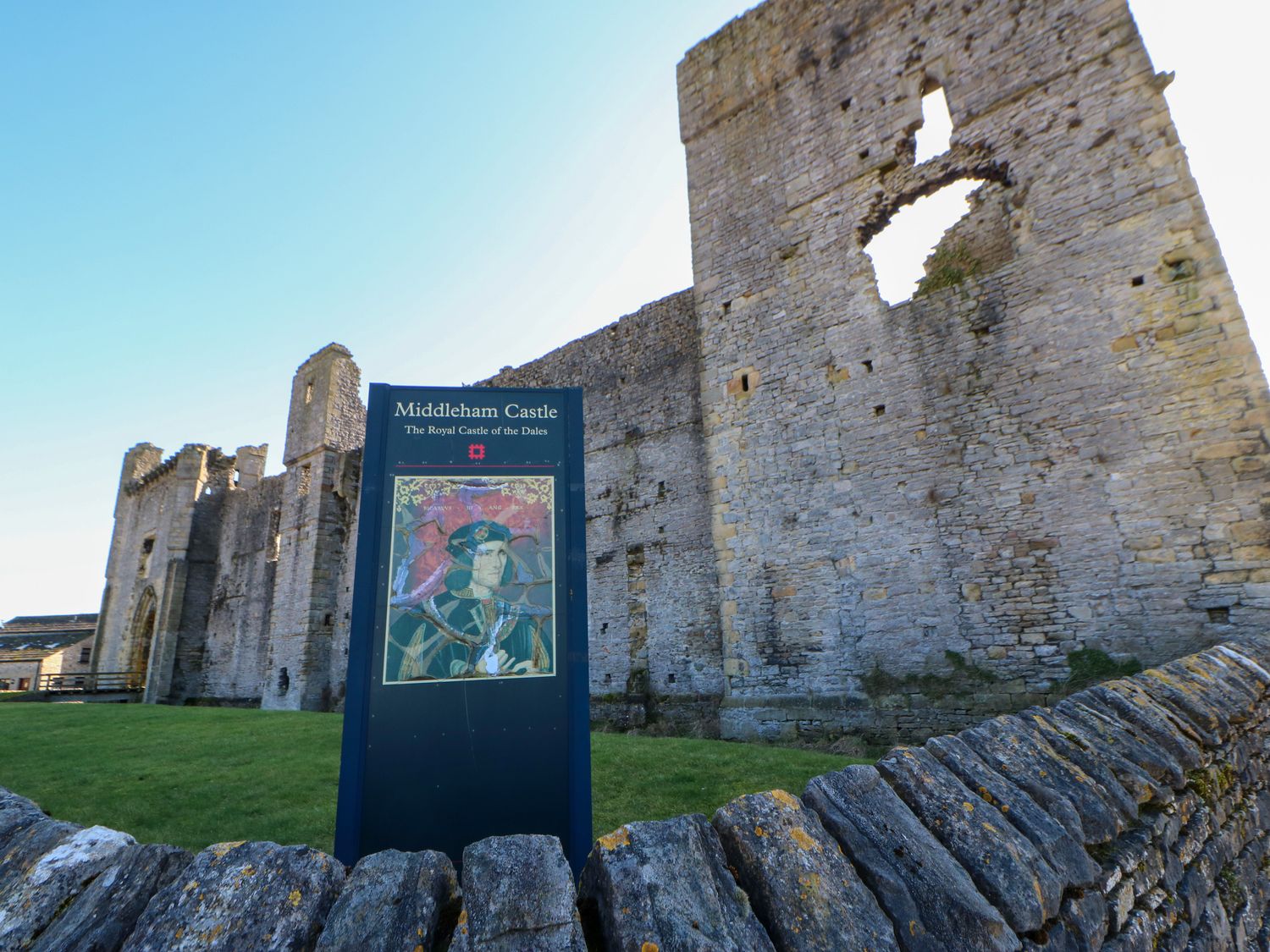 The ruins of Middleham Castle with a sign in front describing it as the Royal Castle of the Dales in Middleham