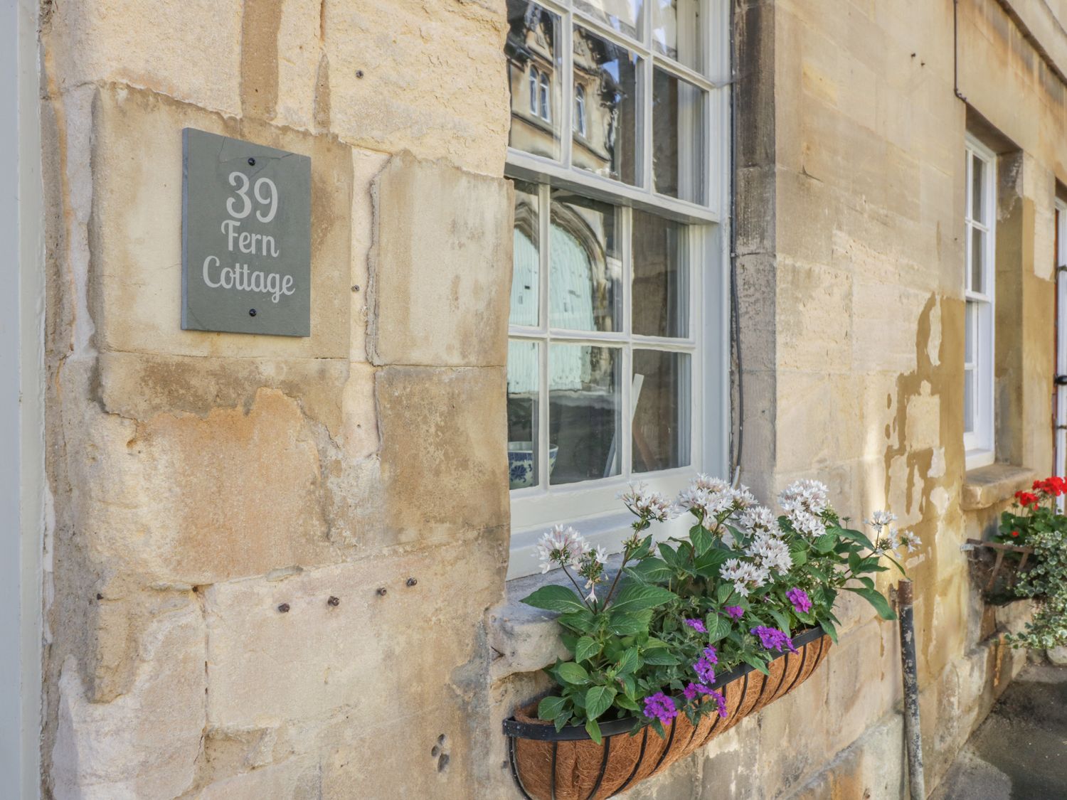 A window with flower boxes on a stone wall next to a Fern Cottage sign at Winchcombe