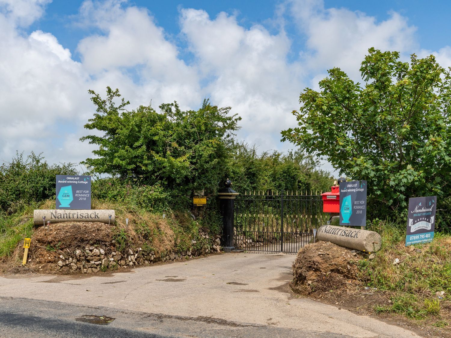 A driveway entrance with stone signs reading Nantrisack and black metal gates surrounded by bushes and trees at Bear Cottage in Chacewater near Truro