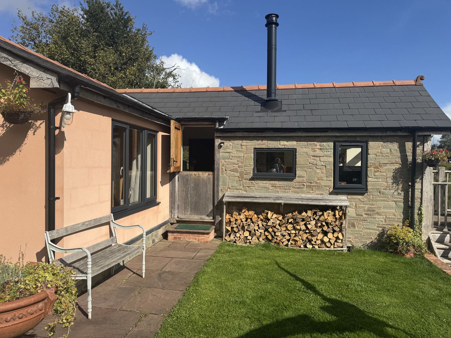 An outdoor view of a cabin with a wood pile and garden at The Hideout in Llangrove