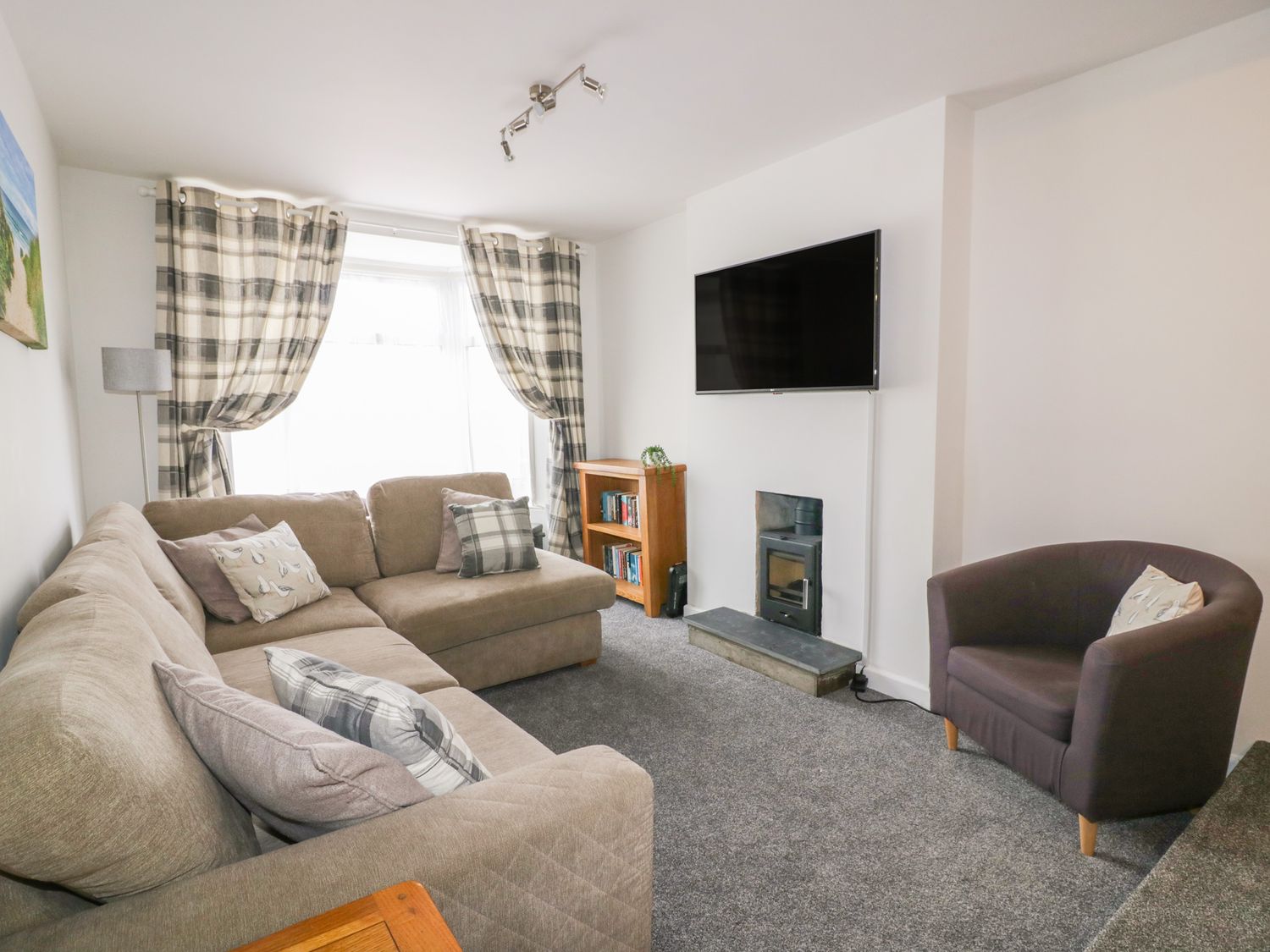 A living room with a sectional sofa armchair wall mounted tv and curtains at Fistral Quay in Newquay