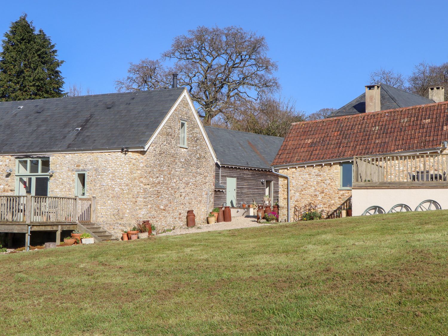 Stone buildings with pitched roofs and wooden decks surrounded by grass and trees at The Shippon at Wyke Farm in Lyme Regis