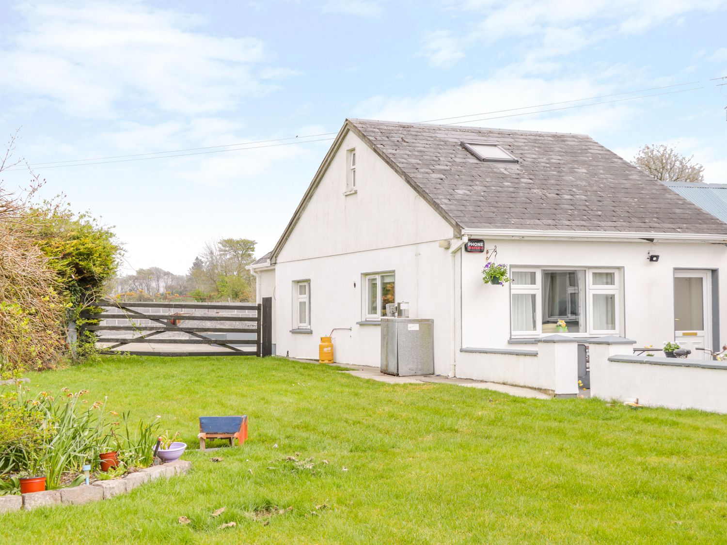 A white house with a sloped roof and a small garden with potted plants and grass surrounded by a black wooden gate at Sunset View in Keelogues near Glenamaddy County Galway