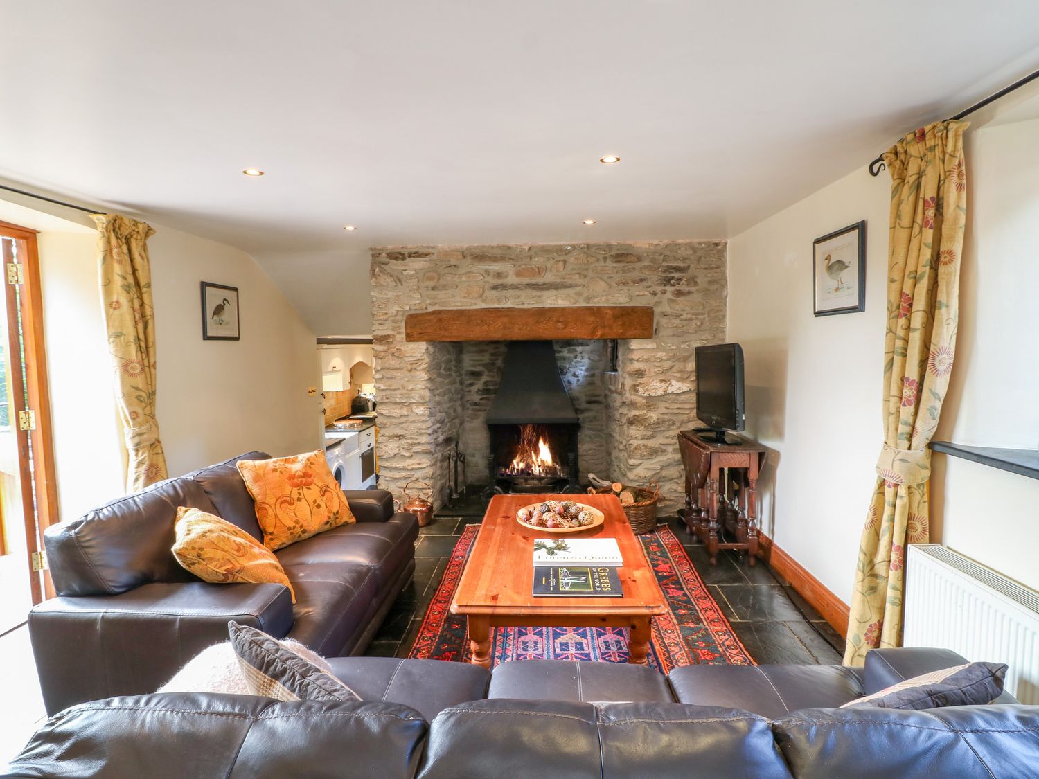 A living room with leather sofas a wooden coffee table a stone fireplace and a television at Great Bradley Cottage in Withypool