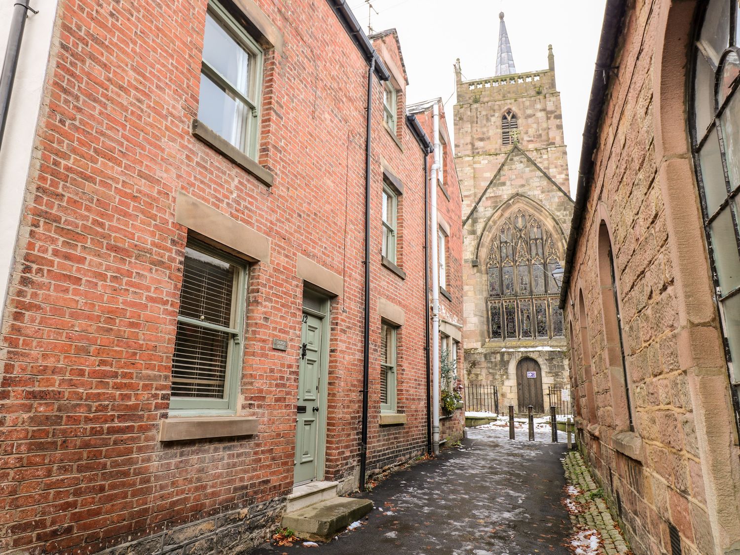 A narrow alley with brick buildings on both sides and a large church with arched windows at Church House in Wirksworth
