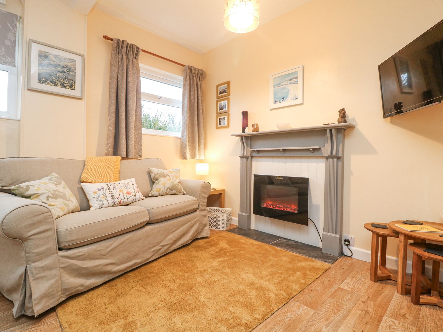 A living room with a beige sofa and pillows a fireplace and a wall mounted television at The Roost in Camborne
