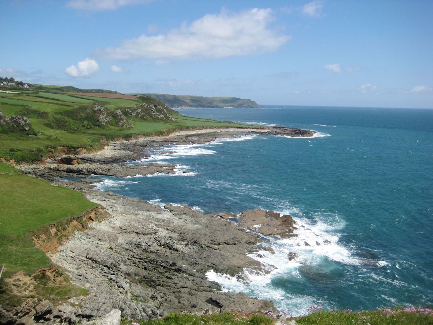 A rocky coastline with green fields and cliffs by the sea at Little Piccadilly in Coles Cross near Kingsbridge