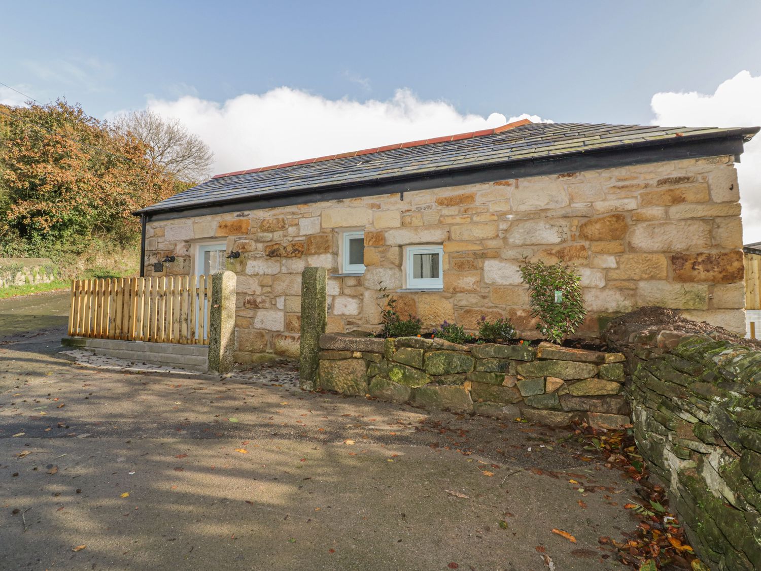 A stone building with two small windows and a wooden fence on the side at The Bull Pen in Coombe near Grampound