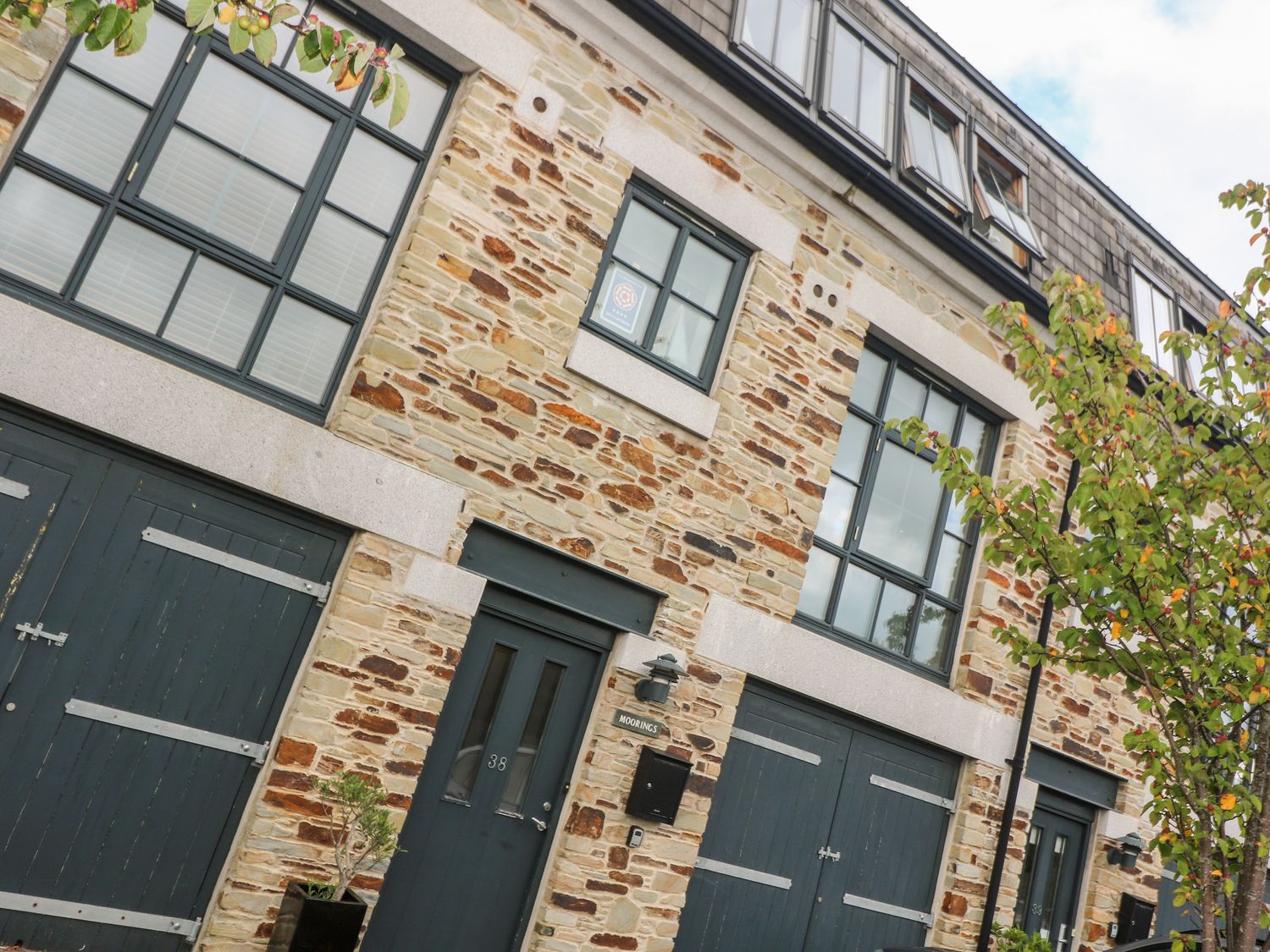 A stone building with dark green doors and windows and a tree in front at The Moorings in Lostwithiel