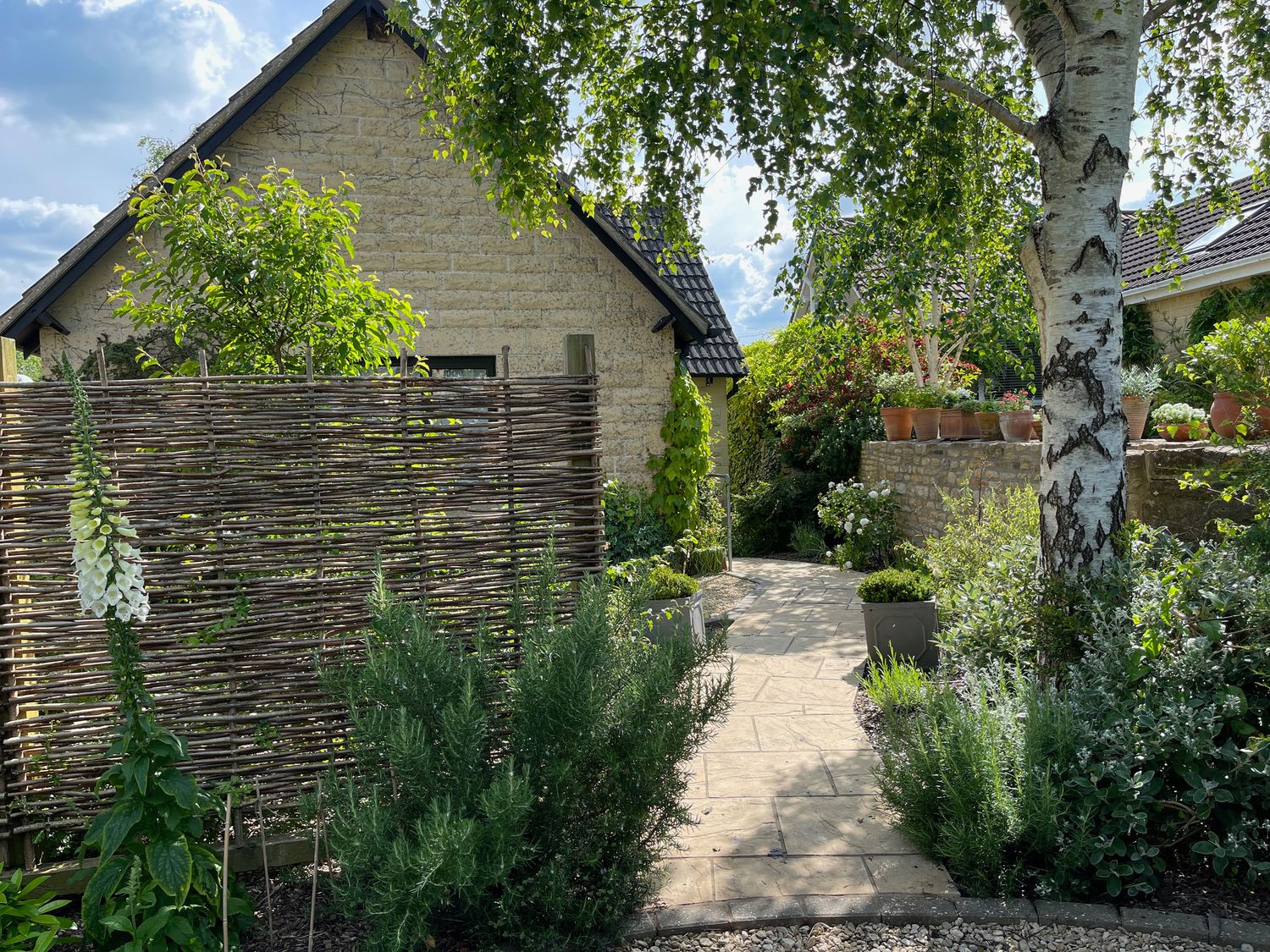 A garden pathway with plants and trees next to a stone house at 1A Erneston Crescent in Corsham