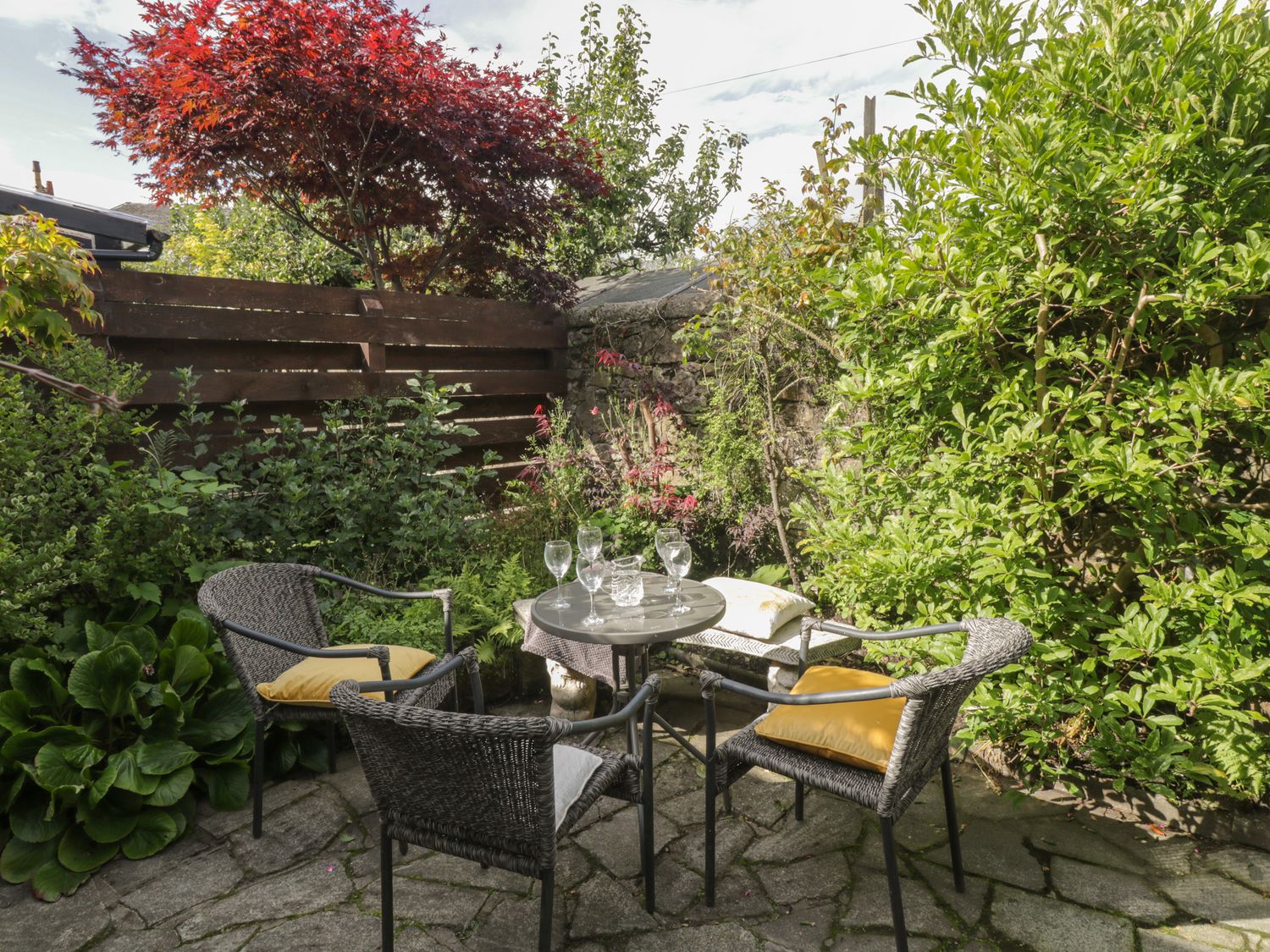 An outdoor seating area with four chairs around a small table and various plants and trees at 6 Ronald Place in Stirling