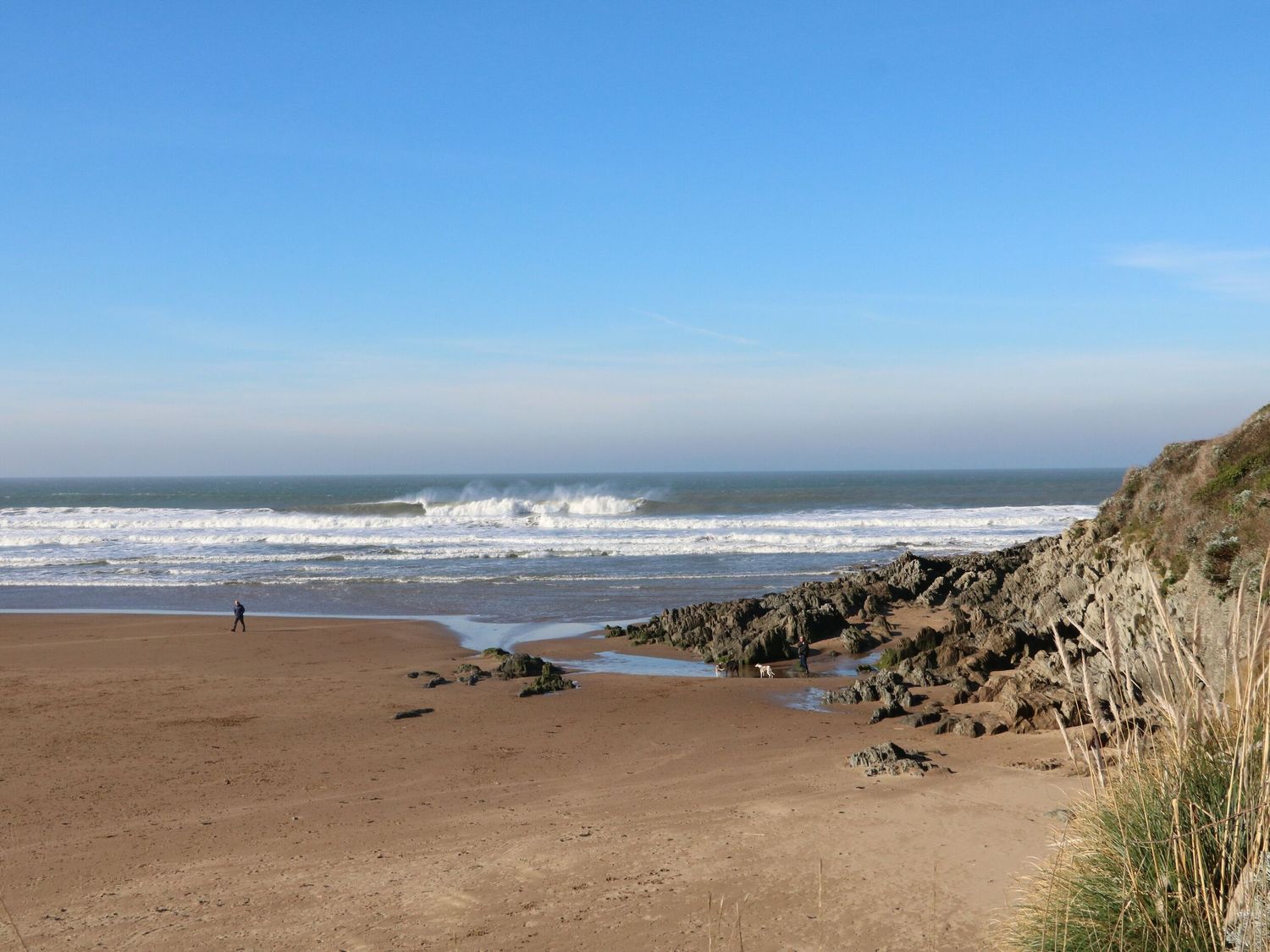 A sandy beach with rocks and waves of the ocean under a clear sky at Rosebank Cottage in Mortehoe