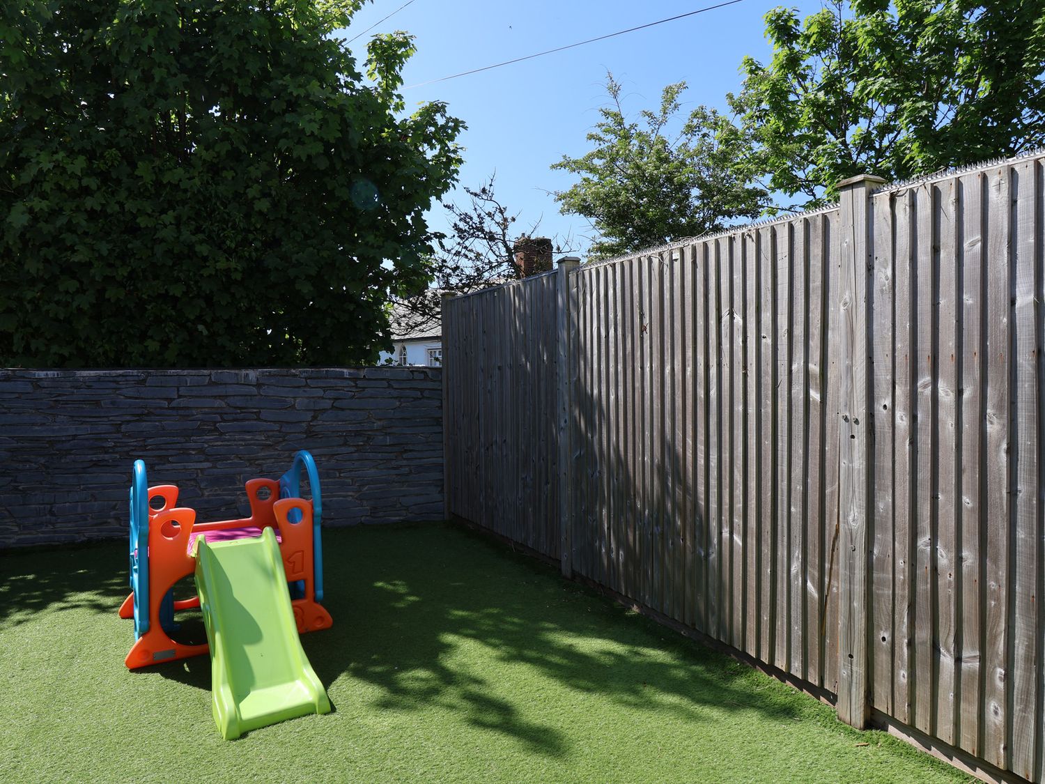 A small playground with a plastic slide on artificial grass surrounded by wooden and stone fences at Rosebank Cottage in Mortehoe