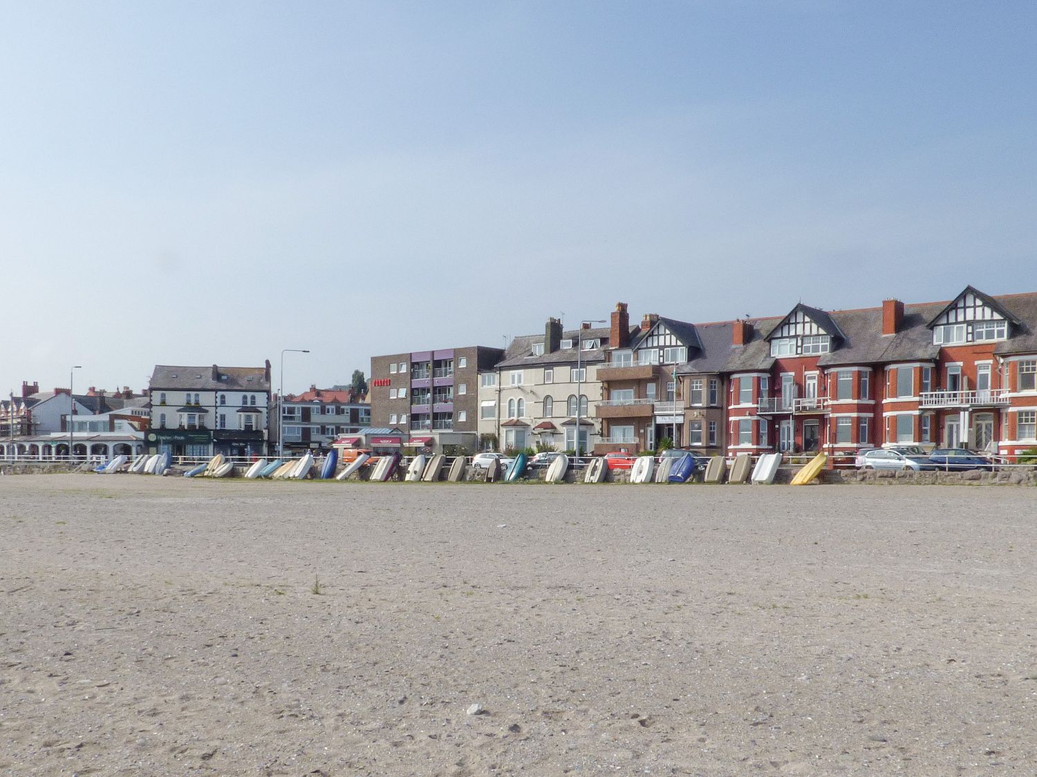 A row of small boats lined up on a sandy beach with buildings behind at The Yatt in Rhos-On-Sea