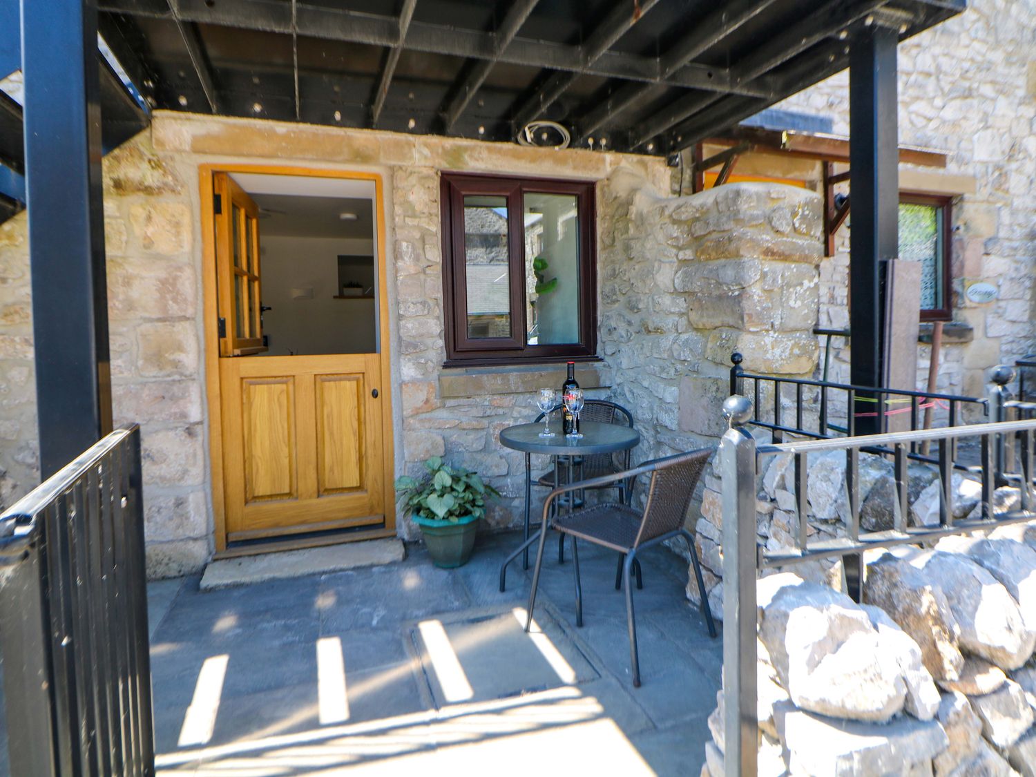 A stone patio with a round table and two chairs next to a wooden door and window at The Nest in Cowdale near Buxton