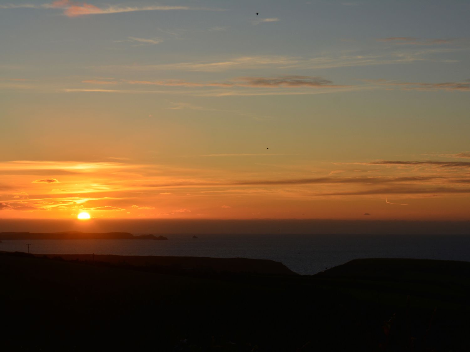 A sunset over the ocean with a mostly clear sky and some clouds at Glenhaven in Trewarmett near Tintagel