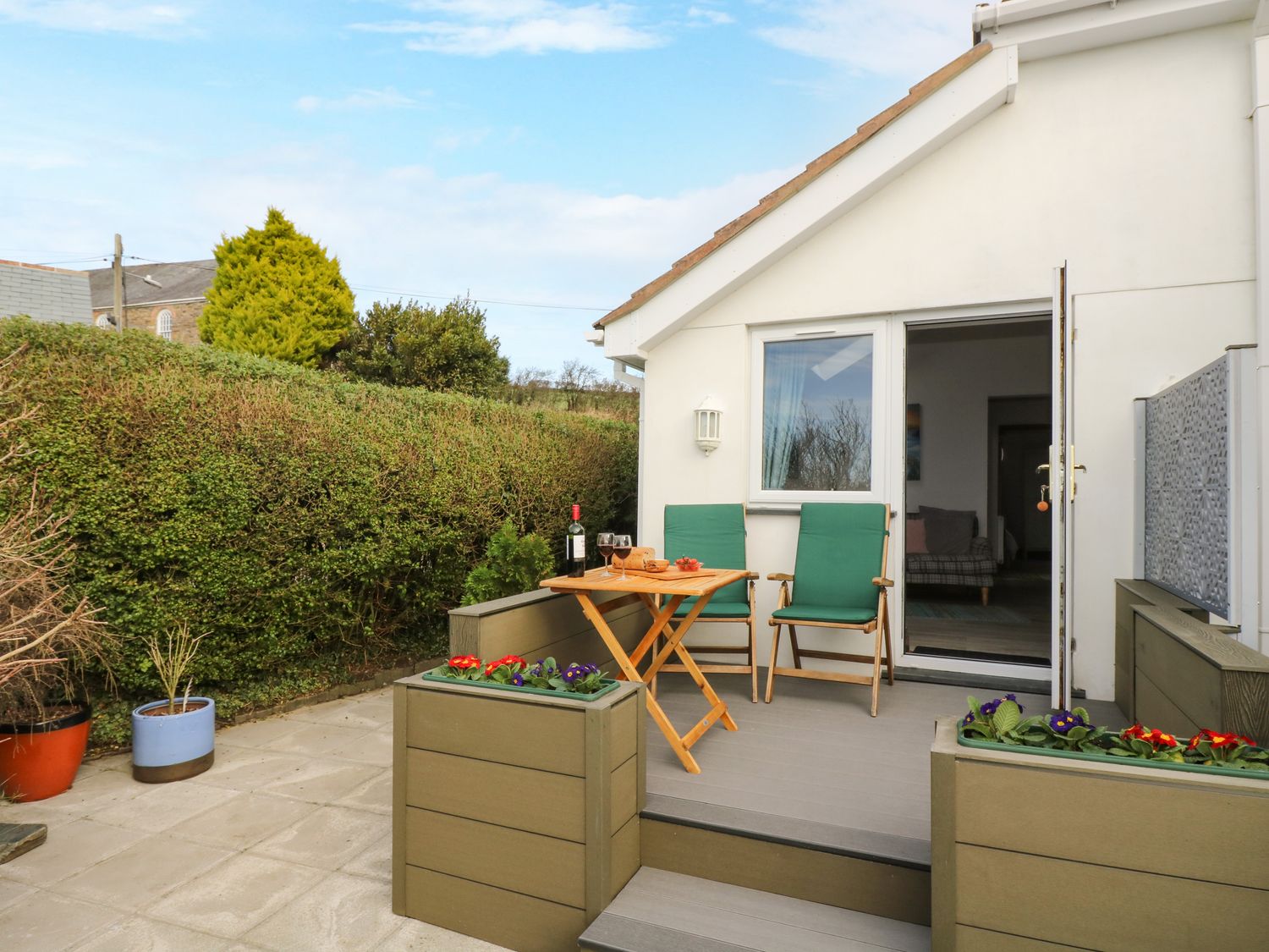 A patio with two green chairs and a wooden table with wine glasses outside a white house at Glenhaven in Trewarmett near Tintagel