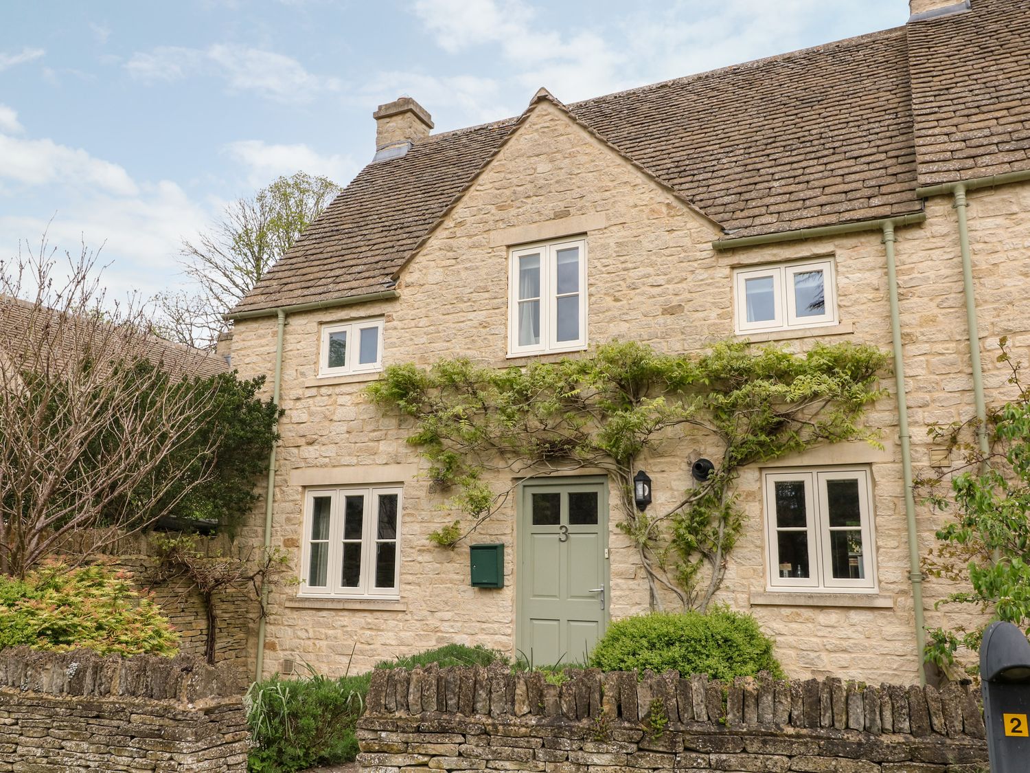 A stone house with green door and windows with plants on the facade at 3 Painters Field in Quenington Near Cirencester
