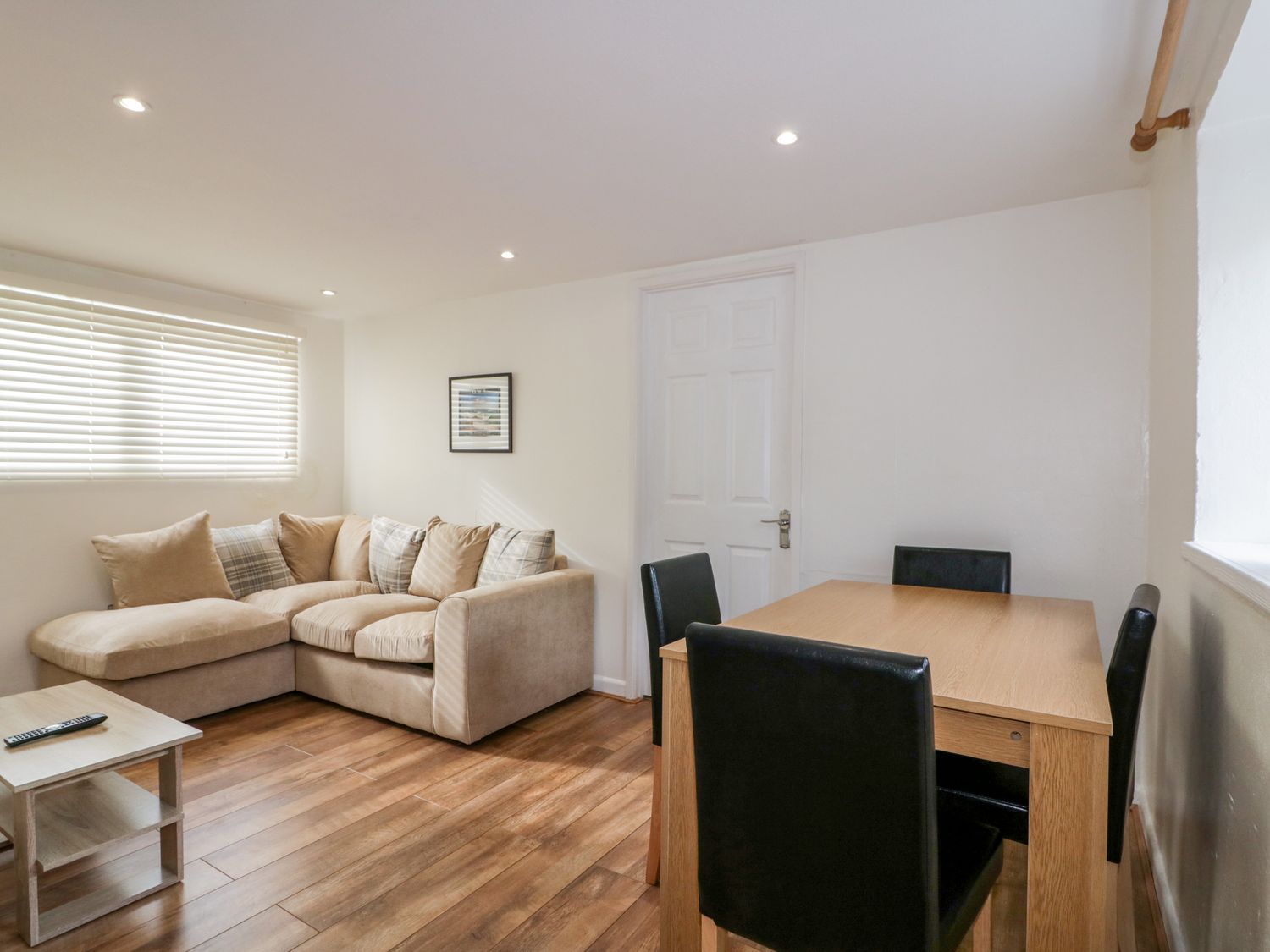A living room with a beige sofa a wooden table with black chairs and a small wooden coffee table at Cove Cottage in Tintagel