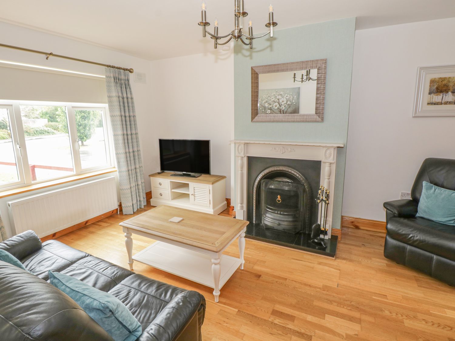 A living room with two leather sofas a wooden coffee table a television on a stand and a fireplace with a mirror above at Duffy's Cottage in Gorteen County Sligo