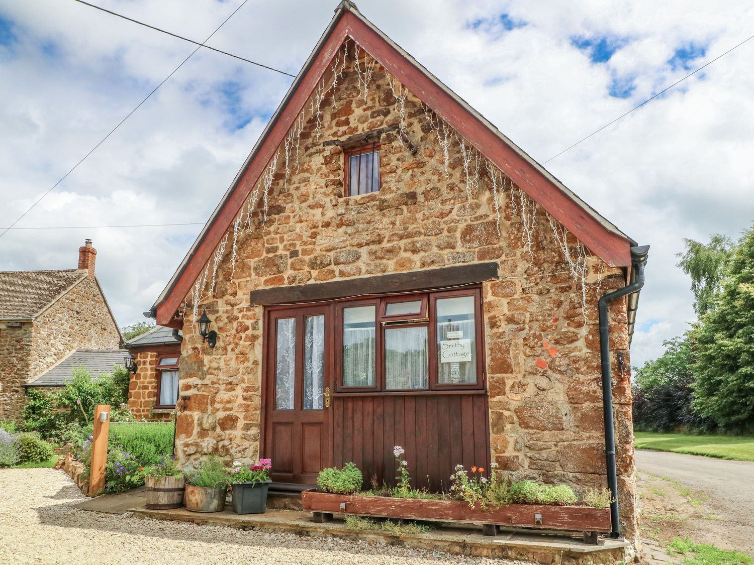 A stone cottage with wooden door and windows and flower pots outside at The Forge at Smithy Cottage in Bloxham