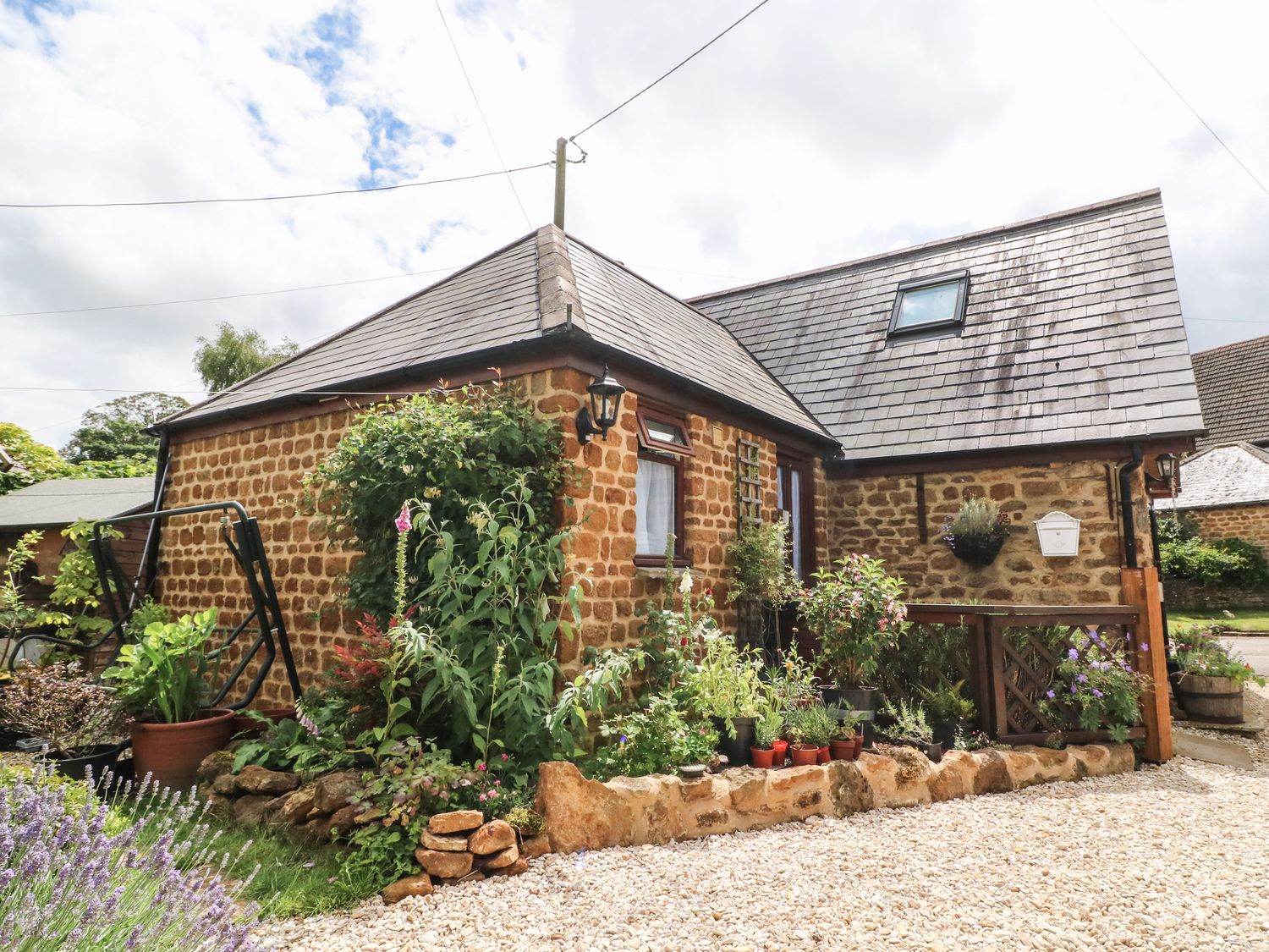 A stone cottage with a garden and potted plants outside at The Forge at Smithy Cottage in Bloxham