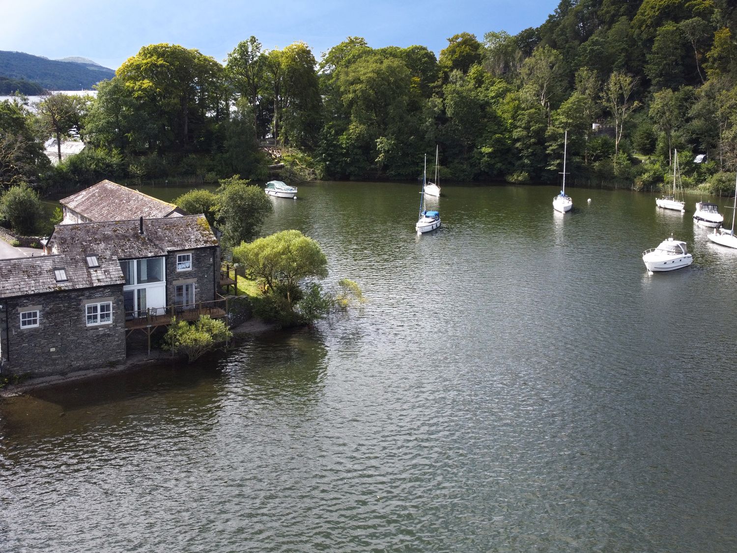 A stone house on the water with several boats moored and trees surrounding the area at Lund in Far Sawrey