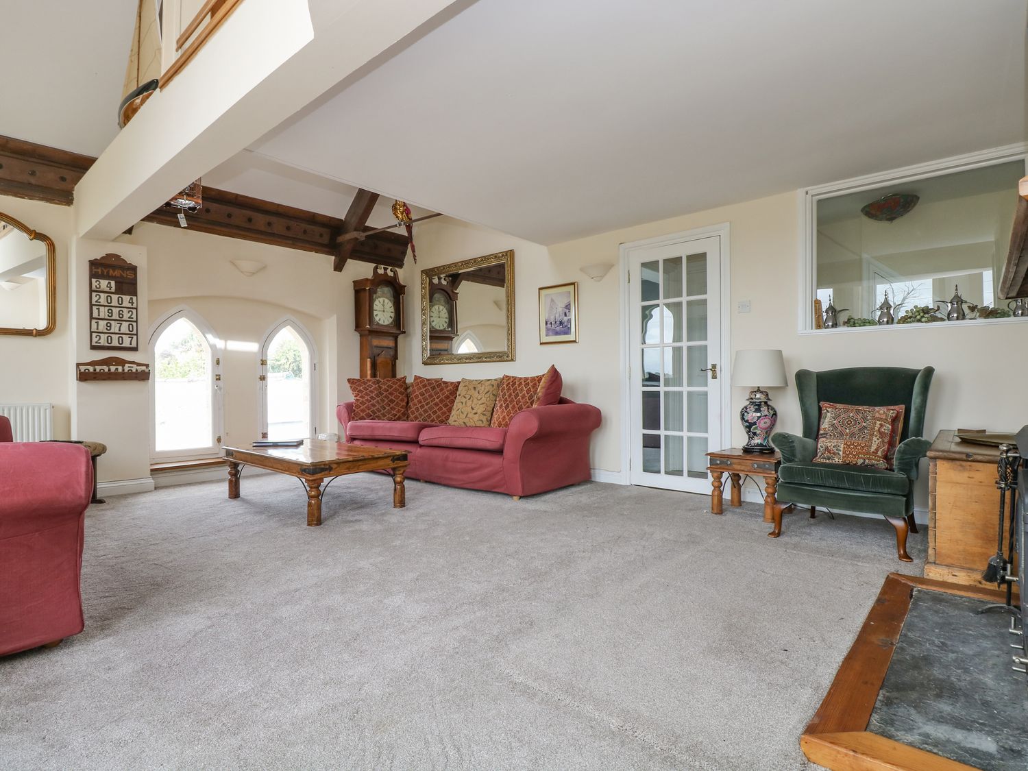 A living room with red sofas a green armchair a wooden coffee table and a grandfather clock at The Old Chapel in Lanteglos Highway near Fowey