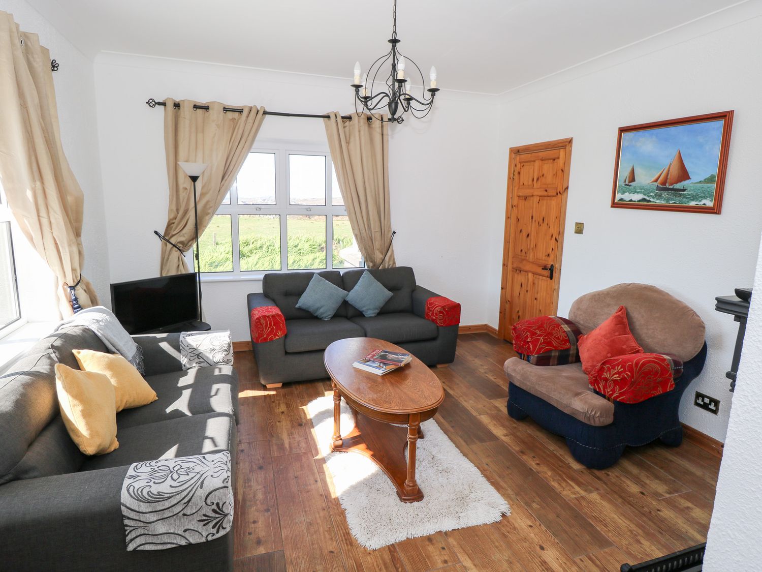A living room with two gray sofas, a brown armchair, a wooden coffee table, a floor lamp, curtains, and a painting at Realt na Maidne in Claddaghduff County Galway