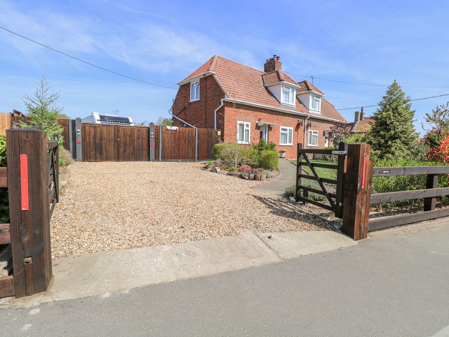 A brick house with a tiled roof behind wooden gates and a gravel driveway at Lillies Pad in Methwold near Feltwell