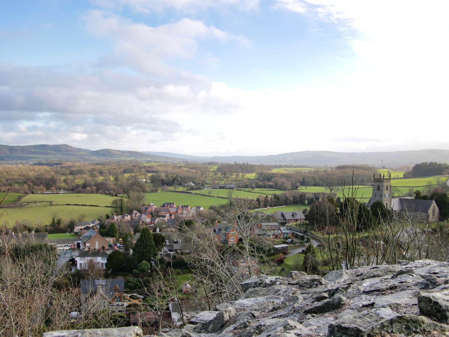 A village with houses and a church surrounded by fields and hills in the background at The Boars Head Pub in Bishops Castle