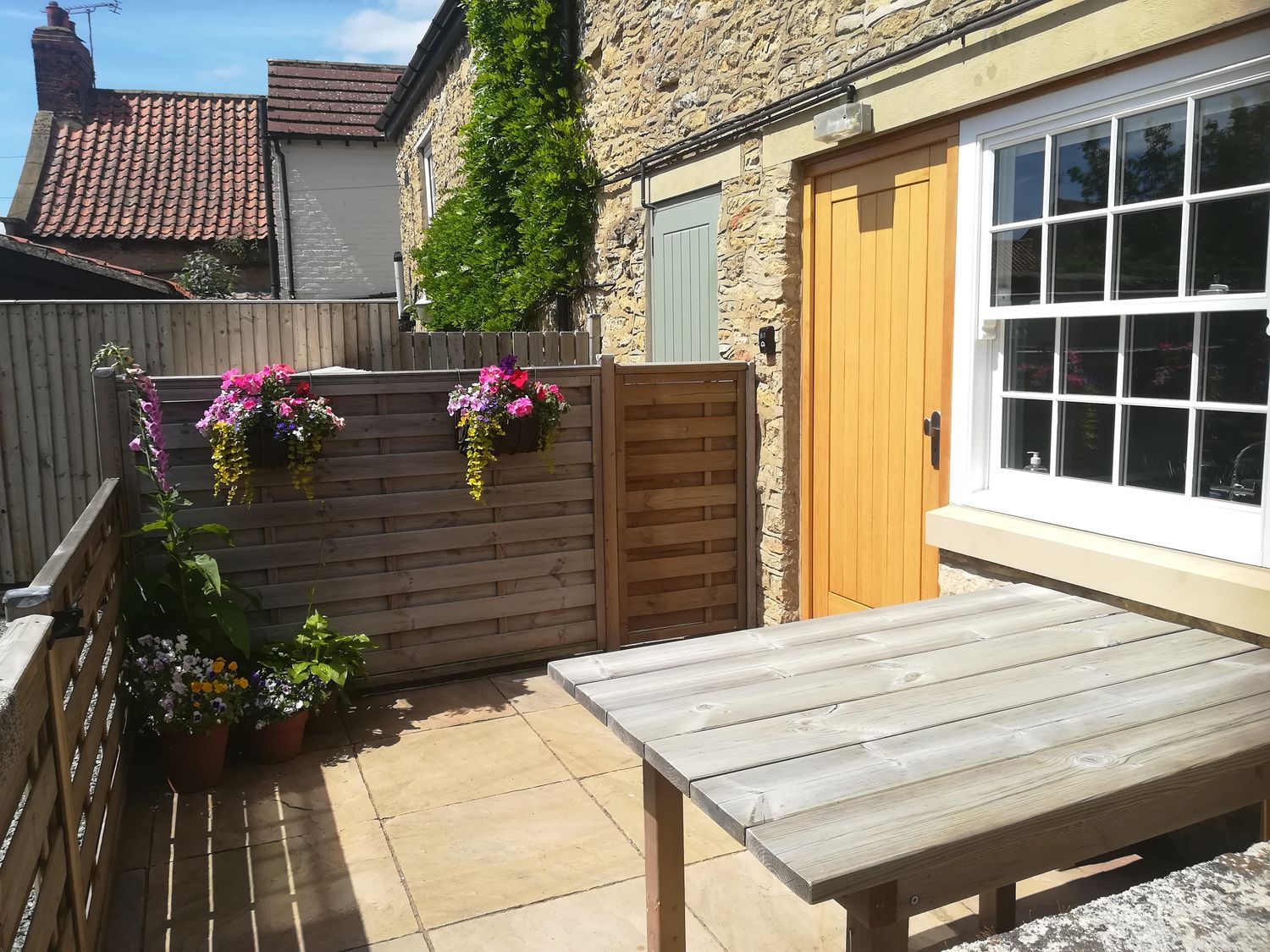 A small patio with a wooden table and flower pots hanging on a wooden fence at May Cottage in Snainton