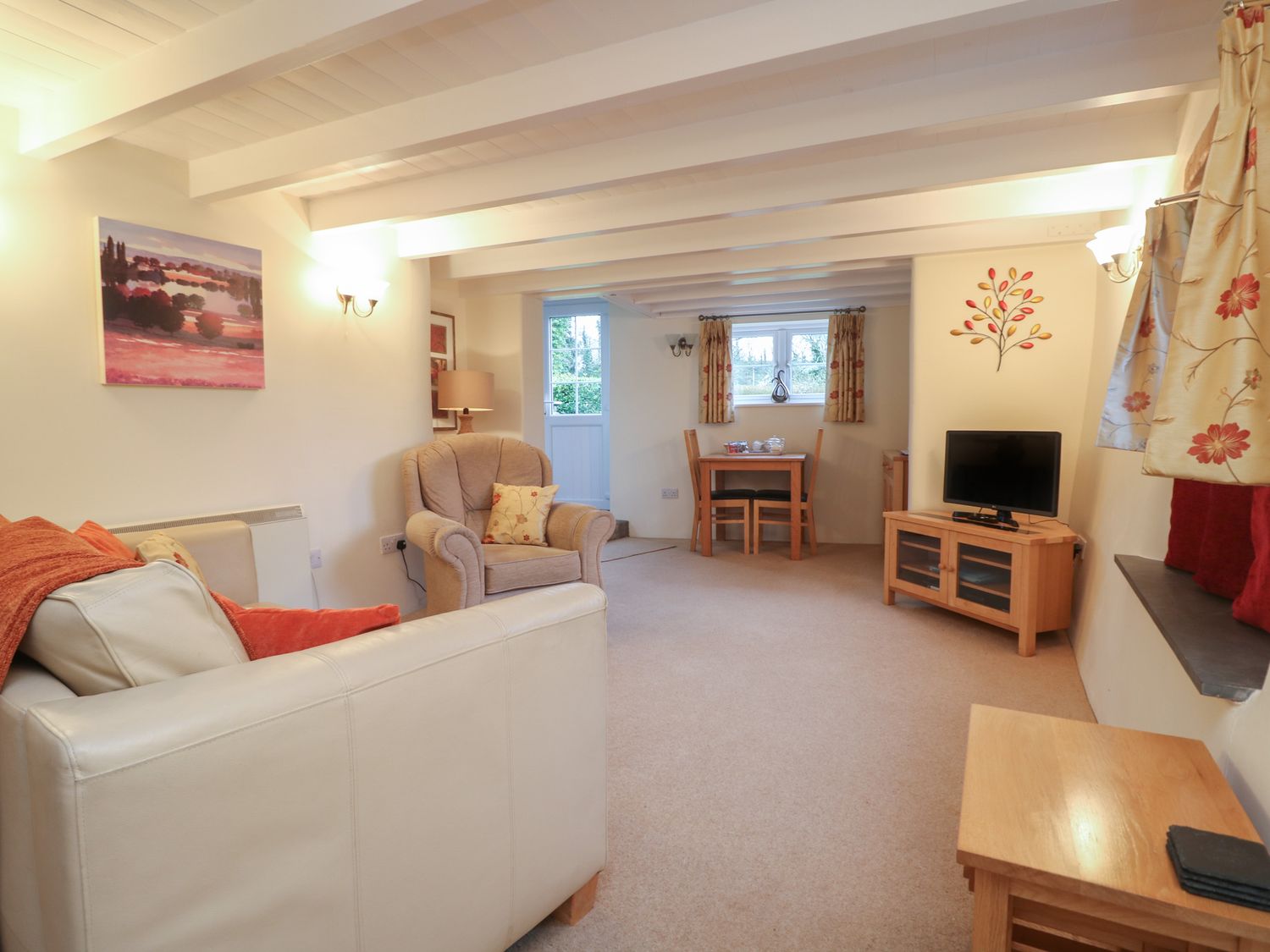 A living room with armchairs a dining table a television and windows at 1 Rose Cottages Lansallos near Polperro