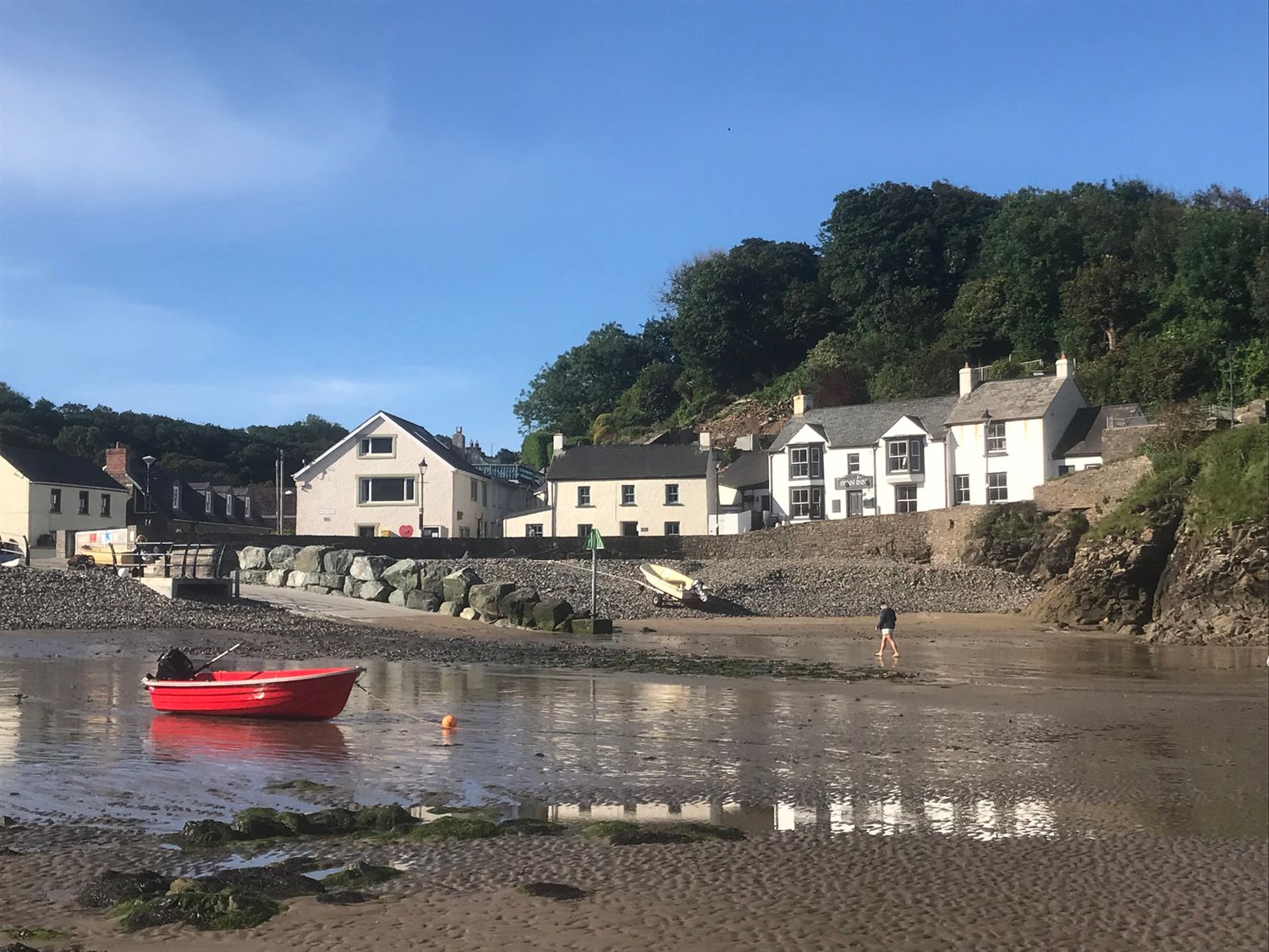 A beach scene with a red boat and houses at Beach Cottage in Little Haven, Pembrokeshire