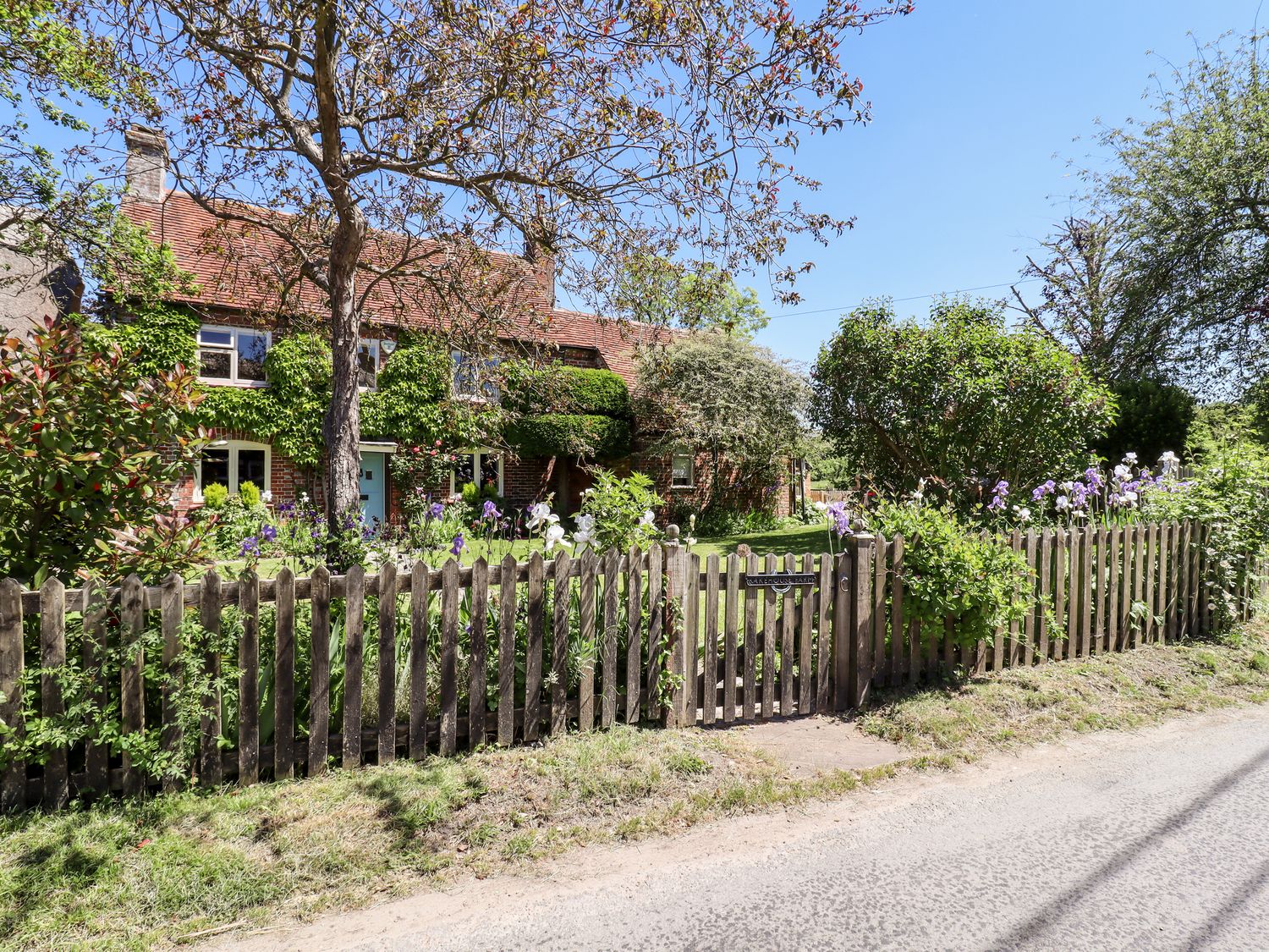 A garden with flowers behind a wooden picket fence and a brick house with a tiled roof in the background at Bakehouse Farm in Bledlow