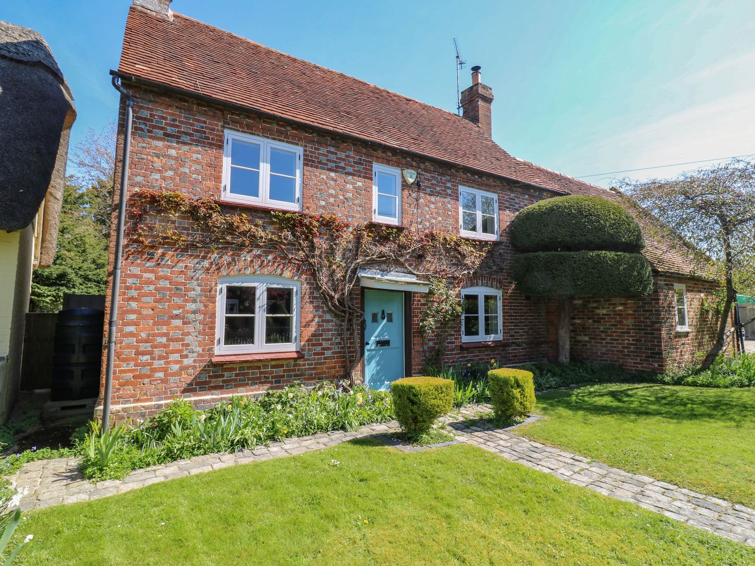 A brick house with a blue door and white windows surrounded by a garden and trimmed bushes at Bakehouse Farm in Bledlow